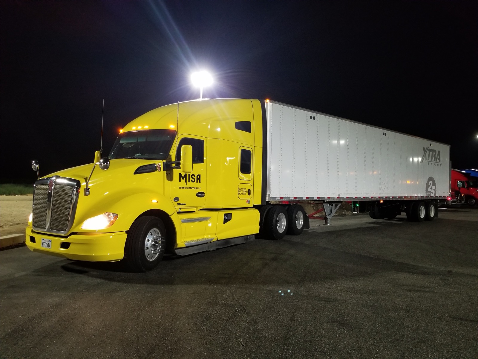 Misa Transportation yellow Kenworth tractor with white dry van trailer at night
